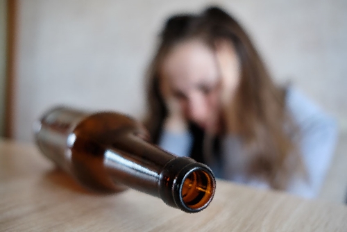A bottle of alcohol on the table and the girl on the background clutched her head.
